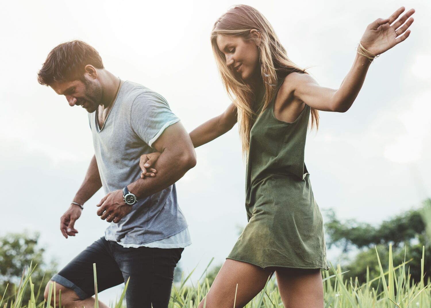 Outdoor shot of young couple walking through meadow hand in hand. Man and woman talking walk through grass field in countryside.